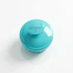 Бірюзова масажна щітка для шкіри голови з логотипом Alopel. Допомагає покращити кровообіг та посилити дію лікувальних засобів.