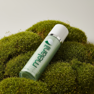 Естетичне фото флакона крему Melanil на зеленому моху, що підкреслює натуральні компоненти засобу.