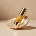 Естетичне фото флакона антивікової сироватки Retorna на мушлі, що демонструє золотисту текстуру засобу.