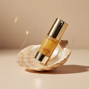 Естетичне фото флакона антивікової сироватки Retorna на мушлі, що демонструє золотисту текстуру засобу.