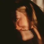 Портрет усміхненої жінки, обличчя якої освітлене природним сонячним світлом, що створює контрастні тіні. Ілюстрація догляду за пігментованою шкірою.